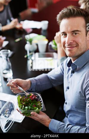 Eating right during the workday. Portrait of a young office worker eating lunch with coworkers at a boardroom table Stock Photo