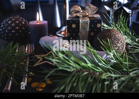 Atmospheric table decoration for a christmas or new year dinner. Place setting in modern style. Gift with golden loop and festive branch decoration, c Stock Photo