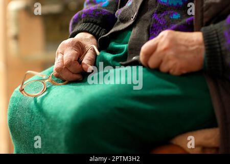 grandmother, white race,she is in a green dress and jacket, communicates with guests,the photo shows the hands of an elderly woman,glasses in one hand Stock Photo
