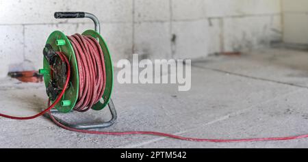 Red and green power cord extension lead drum on construction site ground, closeup detail with empty space for text right side Stock Photo