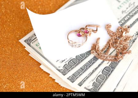 Expensive golden jewerly ring, earrings and necklace with big amount of US dollar bills on luxury glitter golden background surface. Pawnshop or jewer Stock Photo