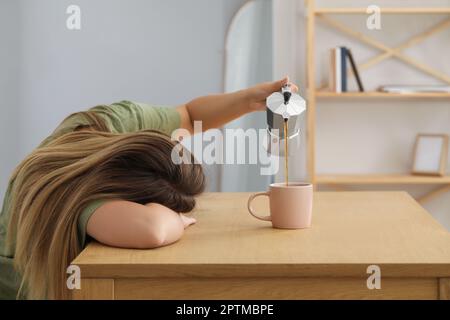 Sleepy woman pouring coffee into cup at wooden table indoors Stock Photo