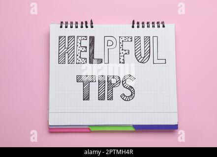 Phrase Helpful Tips in notebook on pink background, top view Stock Photo