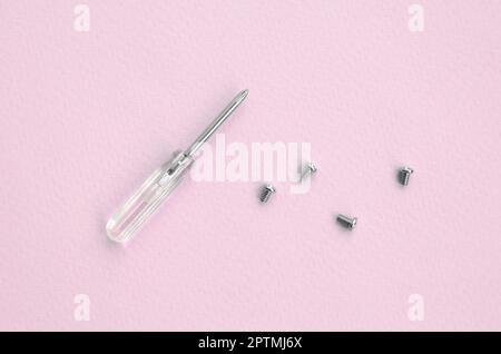 A small screwdriver and a few screws on pink background. Tools for the repair and disassembly of modern smartphones and mobile devices Stock Photo