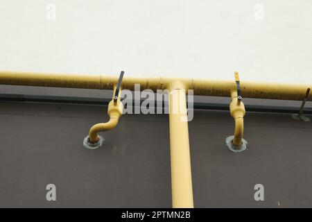 Yellow gas pipes with valves near brown wall outdoors Stock Photo