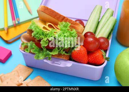 Lunchbox with tasty food and school stationery on light blue background, closeup Stock Photo