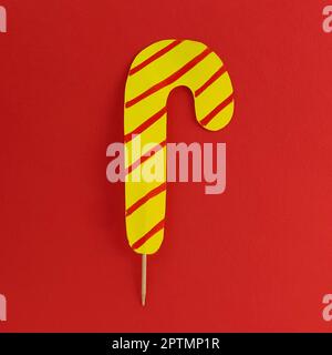 Lollipop on a red background. Imitation of yellow candy with red stripes. New Year or Christmas decoration. Copy space. Lollipop in the middle of the Stock Photo