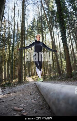 Young woman balancing on wooden log in forest Stock Photo