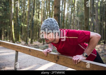 Man doing push-ups on fitness trail in forest Stock Photo