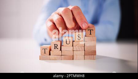 Man's Hand Placing Last Alphabet Of Word Trust Over Wooden Block Stock Photo