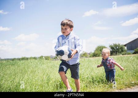 Small boy playing football with his brother on meadow in the countryside, Bavaria, Germany Stock Photo