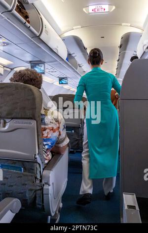 Vietnam Airlines cabin crew taking care of passengers, wearing ao dai uniform on flight from Bangkok to Vietnam Stock Photo