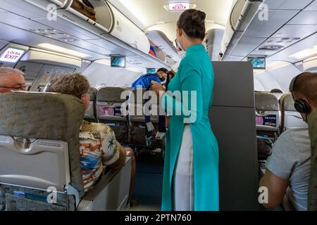 Vietnam Airlines cabin crew taking care of passengers, wearing ao dai uniform on flight from Bangkok to Vietnam Stock Photo