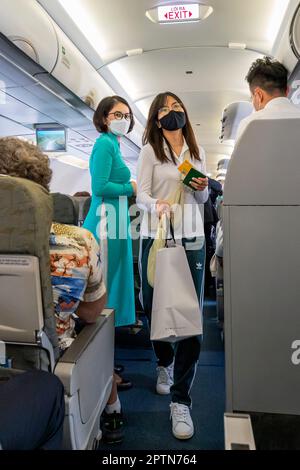 Vietnam Airlines cabin crew taking care of passengers, wearing ao dai uniform on flight from Bangkok to Vietnam Stock Photo