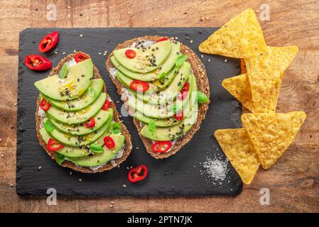 Avocado toasts - bread with avocado slices, pieces of red pepper and sesame on black stone board. Stock Photo