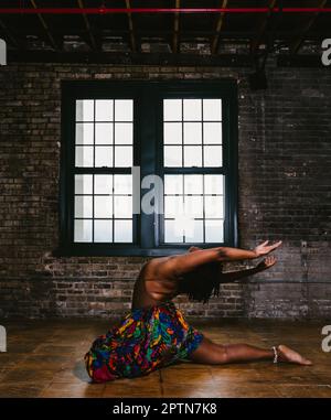 Woman black dancer does back bend in rustic building by window Stock Photo