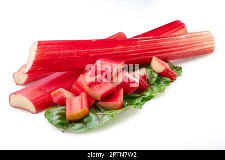 Red rhubarb stems' cuts over rhubarb leaves isolated on white background. Stock Photo