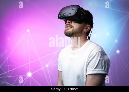 Guy in VR glasses of virtual reality over space gradient colorful background. Enjoying Modern Technologies, Augmented reality, metaverse, game. Hobby Stock Photo