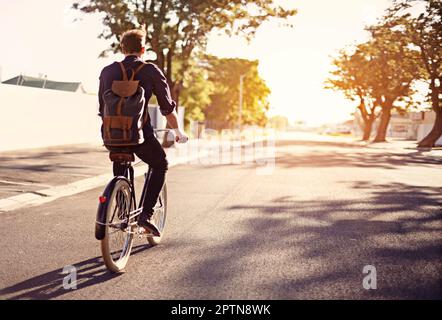 Taking a ride on the brighter side of life. Rearview shot of a young man riding a bicycle outdoors Stock Photo