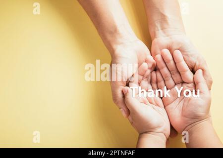 THANK YOU. Family hands holding white thank you text studio shot isolated on yellow background, Mother and child hands hold text message together Stock Photo
