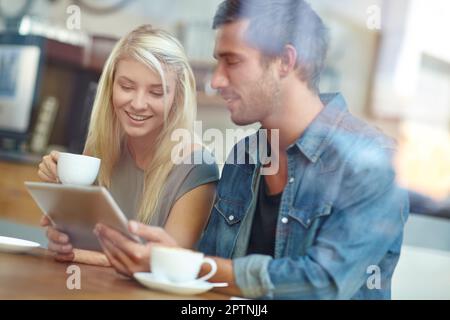 Relaxing together at their favorite coffee spot. a young couple using a tablet while on a coffee date. Stock Photo