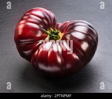 Ripe black or purple tomato on gray slate stone background. Stock Photo