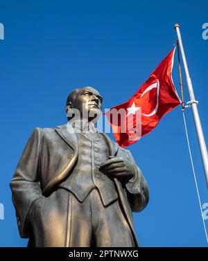 A large bronze statue of Mustafa Kamal Ataturk, the founder of modern Turkey, stands next to a flagpole flying the Turkish flag in a square in Side Ol Stock Photo
