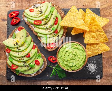Avocado toasts - bread with avocado slices, pieces of red pepper and sesame  on black slate serving plate. Stock Photo