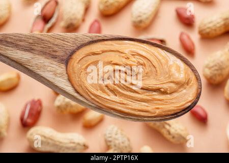 Wooden spoon with peanut butter. Peanuts lay on beige at the background. Top view. Stock Photo