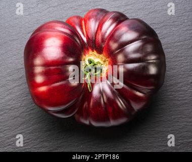 Ripe black or purple tomato on gray slate stone background.  Top view. Stock Photo
