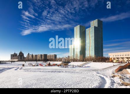 Winter fun park set on the frozen Ishim river in Astana, Kazakhstan. Sun reflects in the glass facade of contemporary high-rise residential buildings Stock Photo