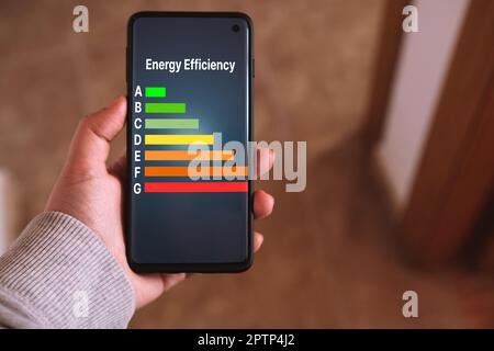 Woman's hand holds a smartphone with a Energy efficiency rating labels on screen. Low consumption and efficient products. Reduce carbon footprint. Stock Photo