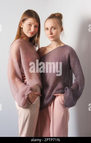 Two pretty girls in thin angora sweater and pants posing near the