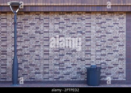 Dark brick wall pattern with chaotic masonry order. Background texture modern stone wall with lamp post and street trash can Stock Photo