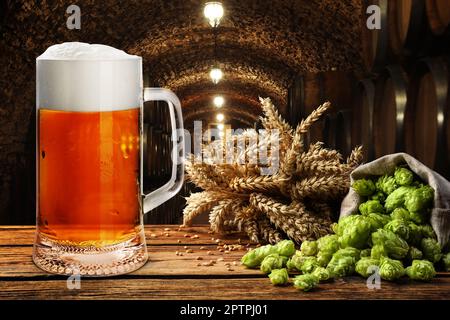 Glass of tasty beer, fresh hops and wheat spikes on wooden table in cellar Stock Photo