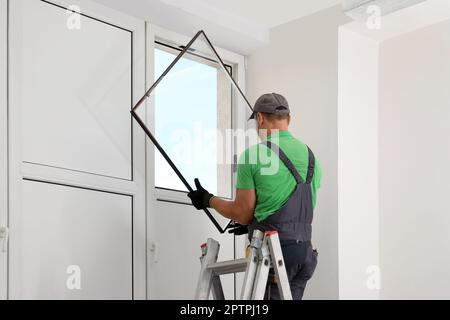 Worker on folding ladder installing window indoors Stock Photo
