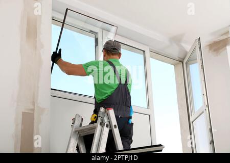 Worker on folding ladder installing window indoors Stock Photo