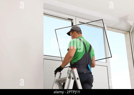 Worker on folding ladder installing window indoors Stock Photo