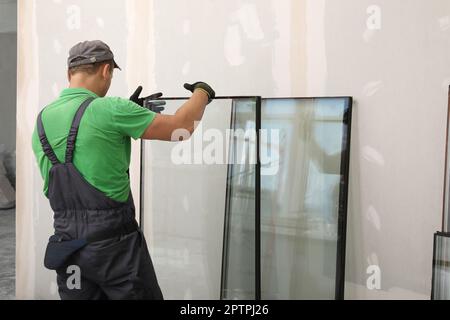 Worker in uniform preparing double glazing window for installation indoors, back view Stock Photo