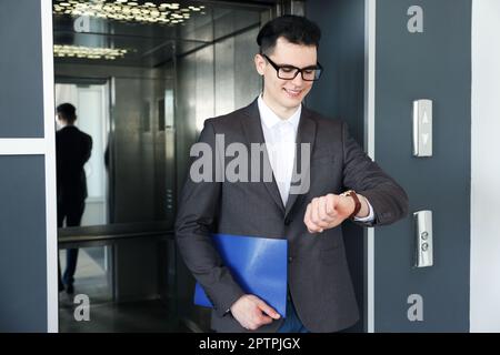 Young businessman walking out of modern elevator Stock Photo