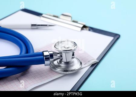 Clipboard with stethoscope and cardiogram on turquoise background, closeup Stock Photo