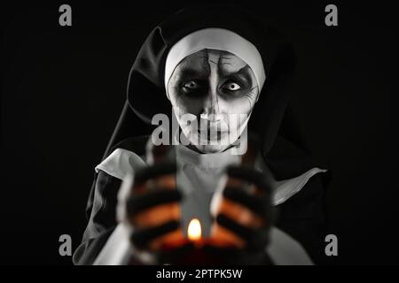 Scary devilish nun with burning candle on black background