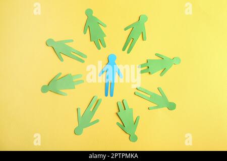 Circle of green paper human figures with blue one in middle on yellow background, flat lay. Diversity and inclusion concept Stock Photo