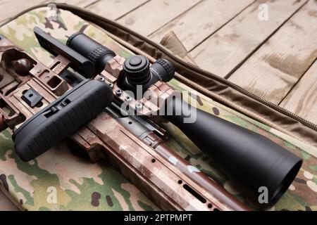 Closeup view of modern powerful sniper rifle with telescopic sight on wooden background Stock Photo