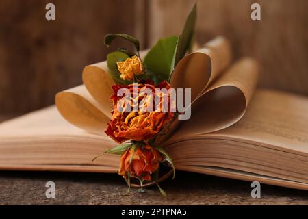 Open book with folded pages and beautiful dried flowers on wooden table, closeup Stock Photo