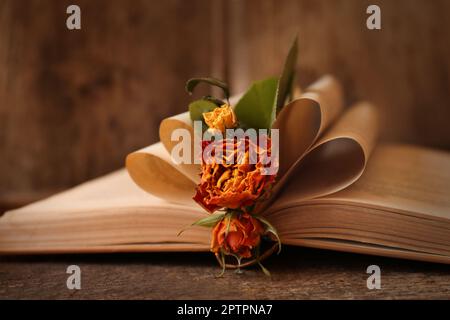 Open book with folded pages and beautiful dried flowers on wooden table, closeup Stock Photo