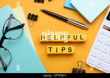 Flat lay composition with phrase Helpful Tips made of yellow cubes on orange background Stock Photo