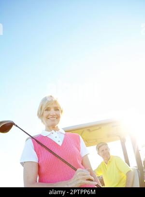Teeing off at tea time. Low angle shot of an attractive older female golfer standing in front of a golf cart with her golfing buddy behind the wheel. Stock Photo