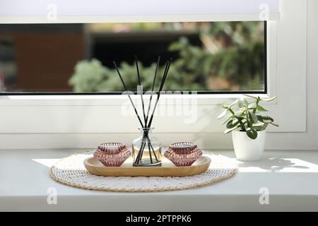Reed diffuser with burning candles and houseplant on white window sill Stock Photo