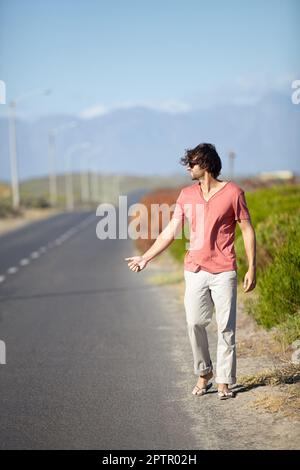 I guess Ill have to hitchhike. A young man trying to hitch a ride while walking along a deserted road Stock Photo